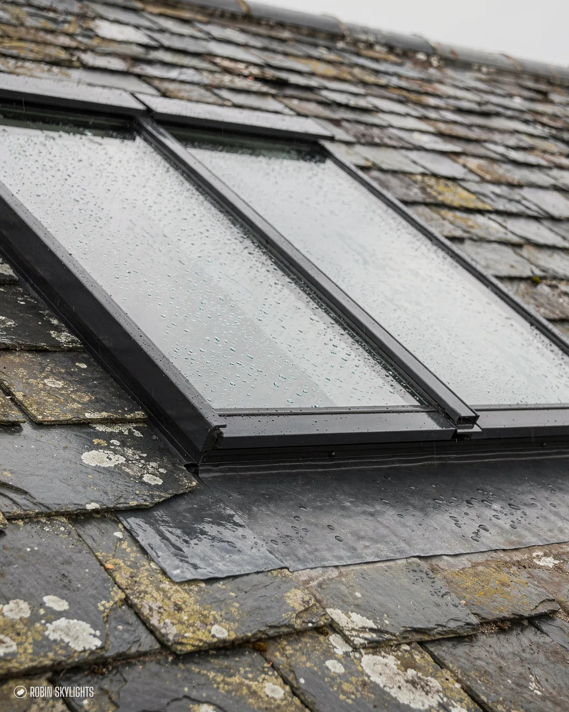 Slim black conservation rooflight with a central bar in an old slate roof