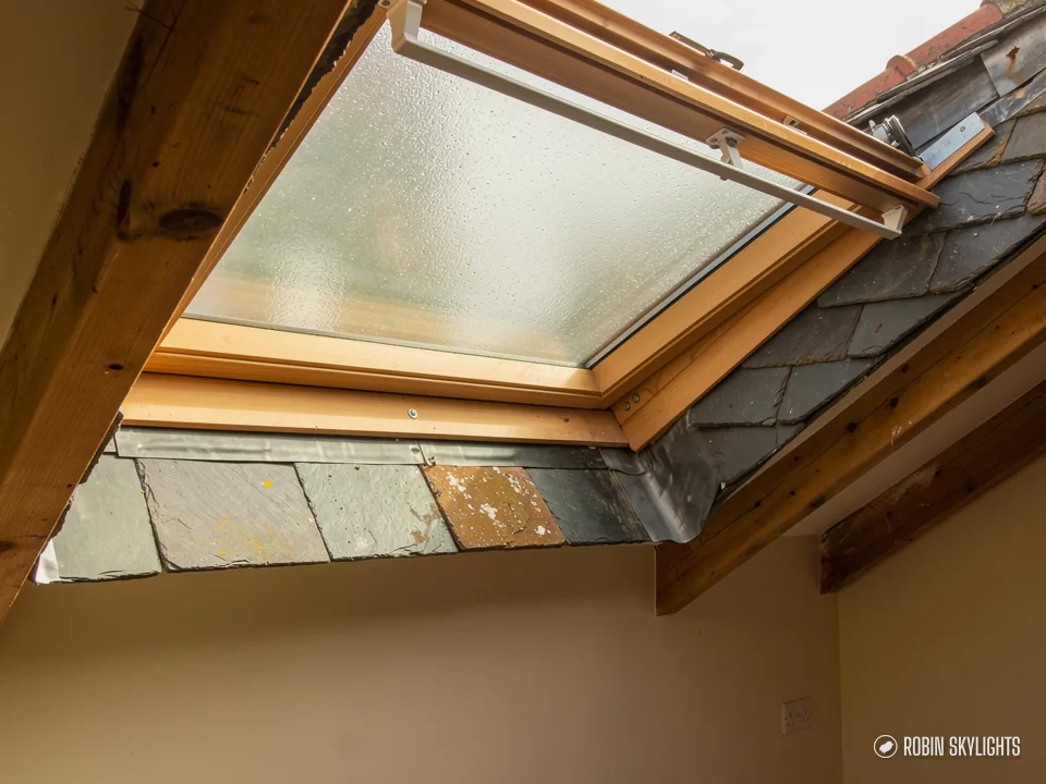 Old pine roof window with clouded glass opened in an unfinished slate roof opening