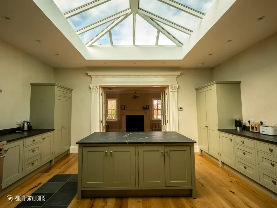 Sage green kitchen with an island lit by a roof lantern overhead