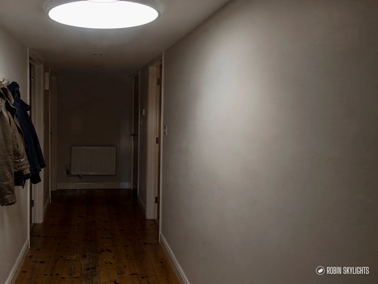 Long hallway with coats on hooks and a round ceiling diffuser