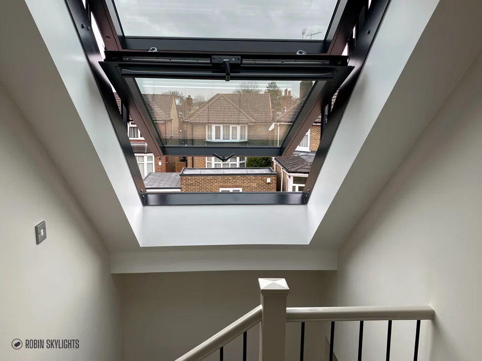 Opened roof window seen from below, framing sky and treetops