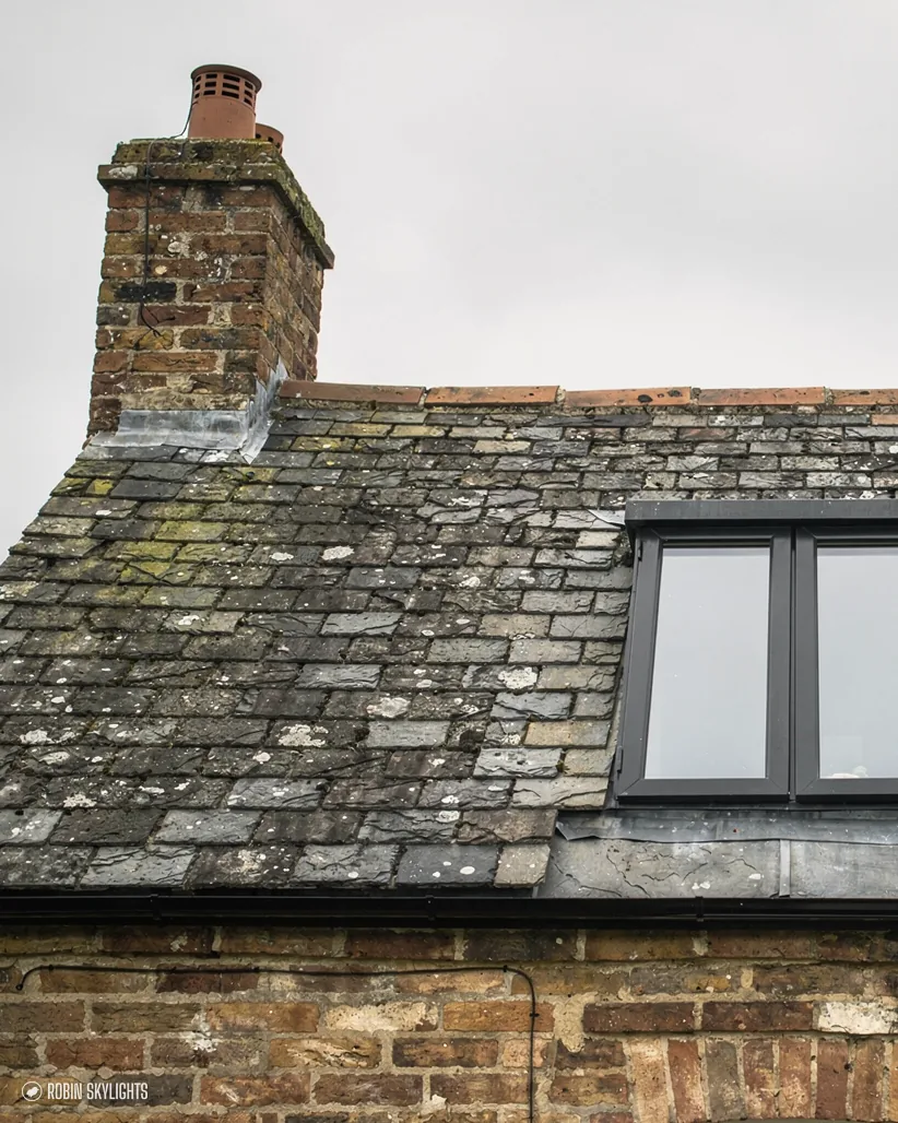 Roof window in an old stone slate roof by a chimney