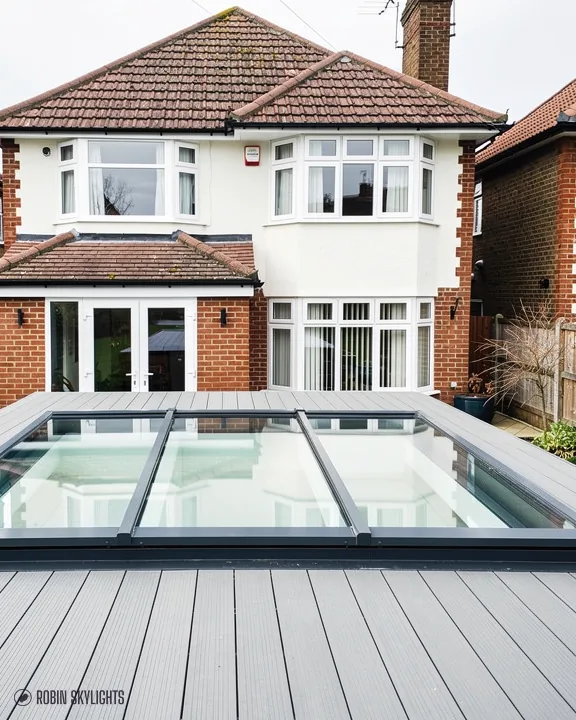 Large glazed rooflight set into grey decking behind a detached house
