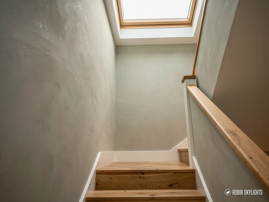 Narrow staircase with a timber handrail lit by a rooflight