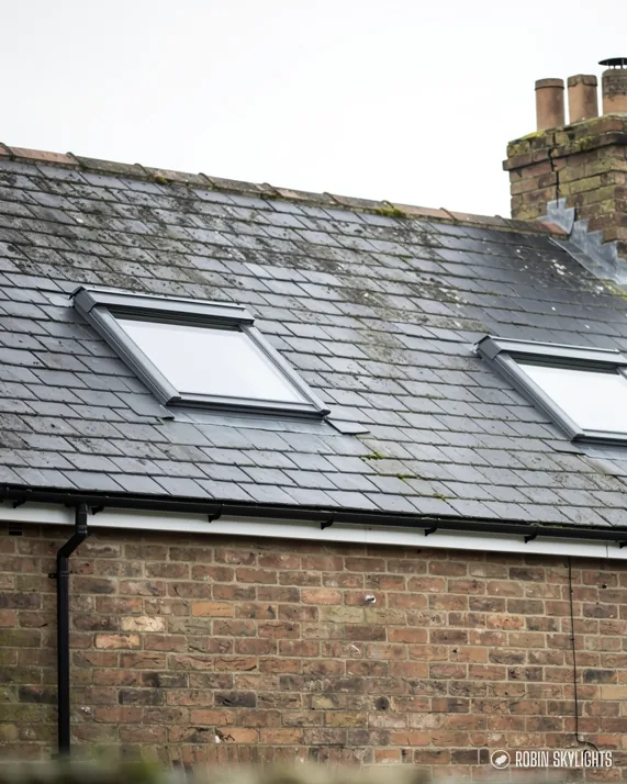 Two roof windows in a slate roof above a brick wall