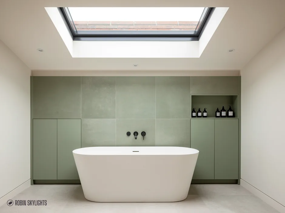 Freestanding bath against green panelling under a flat rooflight