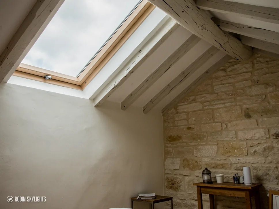 Room with a stone wall and timber beam lit by a roof window