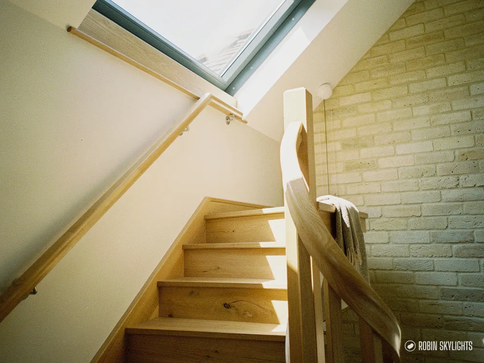 Narrow wooden staircase lit by a roof window above