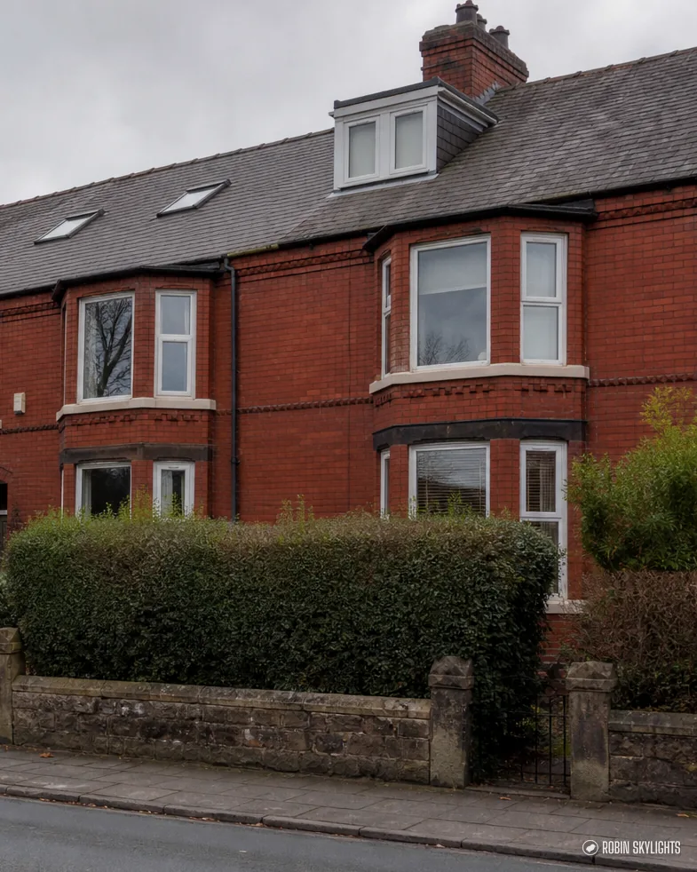 Red brick terraced houses with bay windows and roof windows behind a hedge