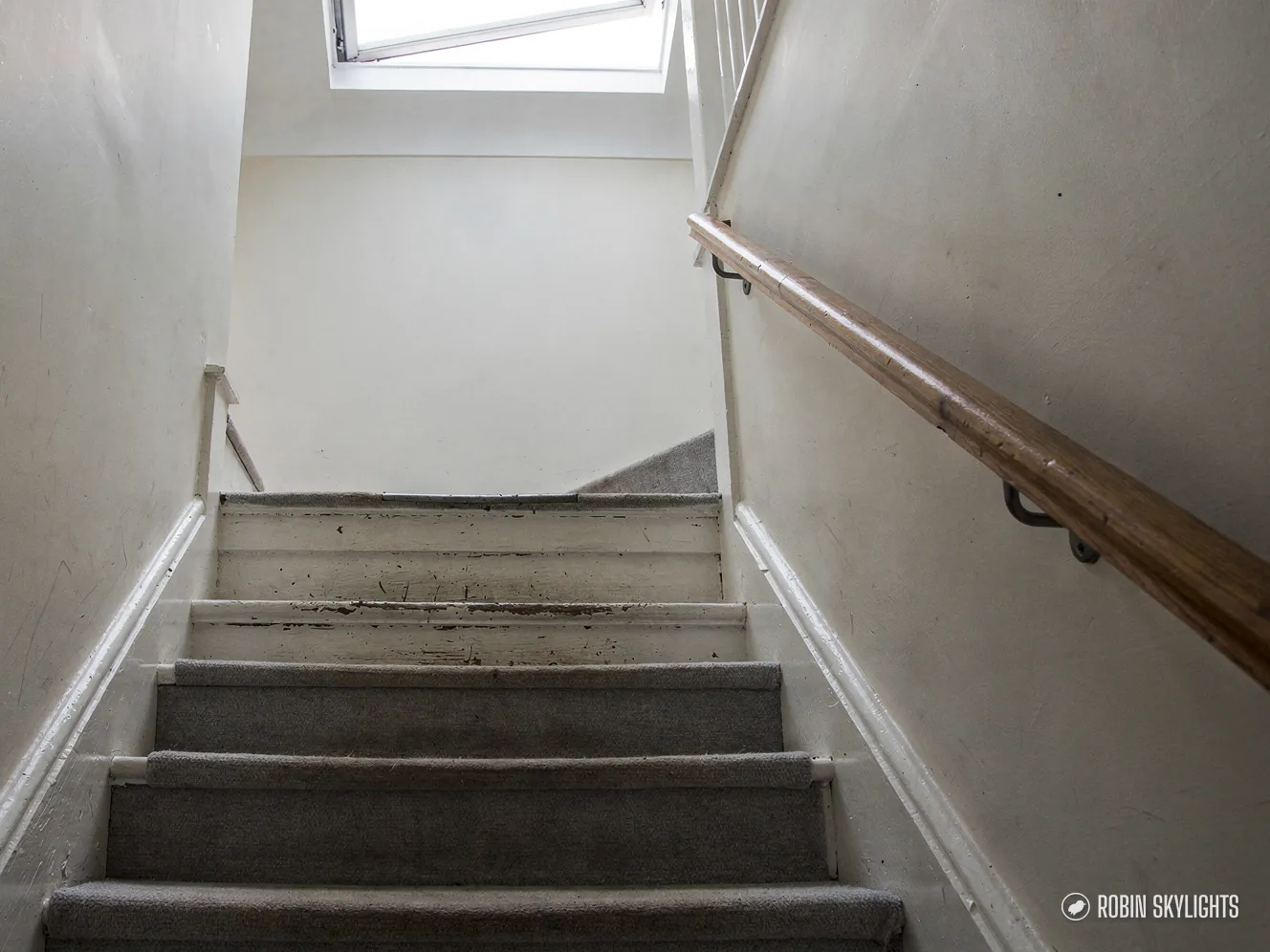 Carpeted staircase with a handrail lit by a rooflight above
