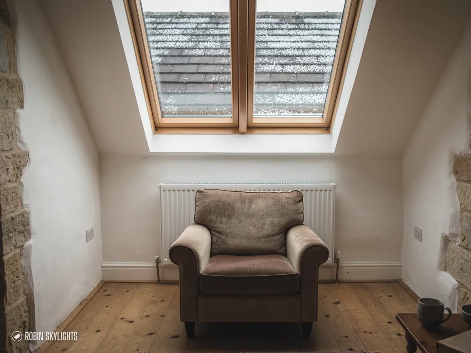 Armchair beneath two roof windows in a room with a stone wall