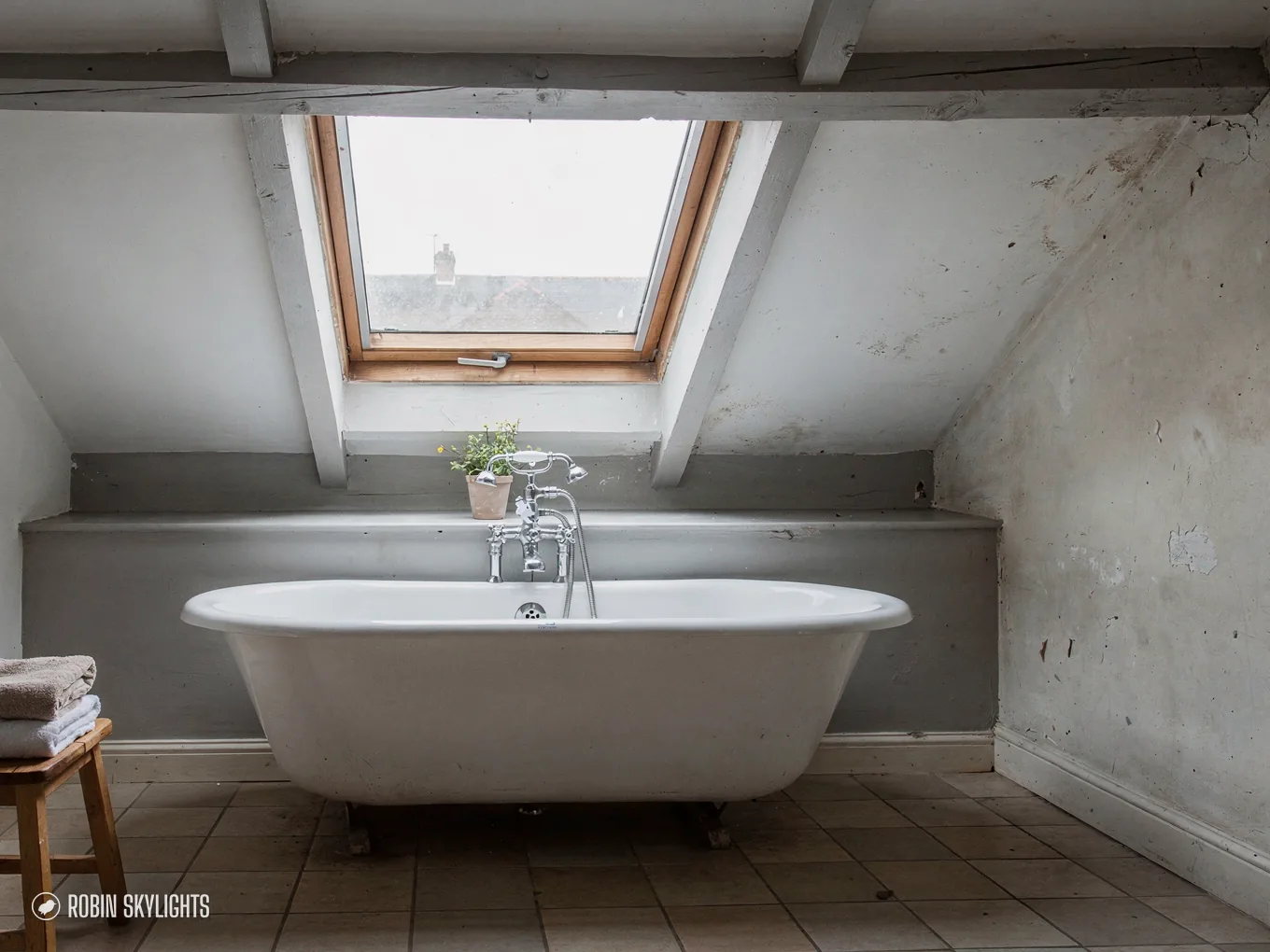 Roll-top bath under a roof window in a grey loft bathroom