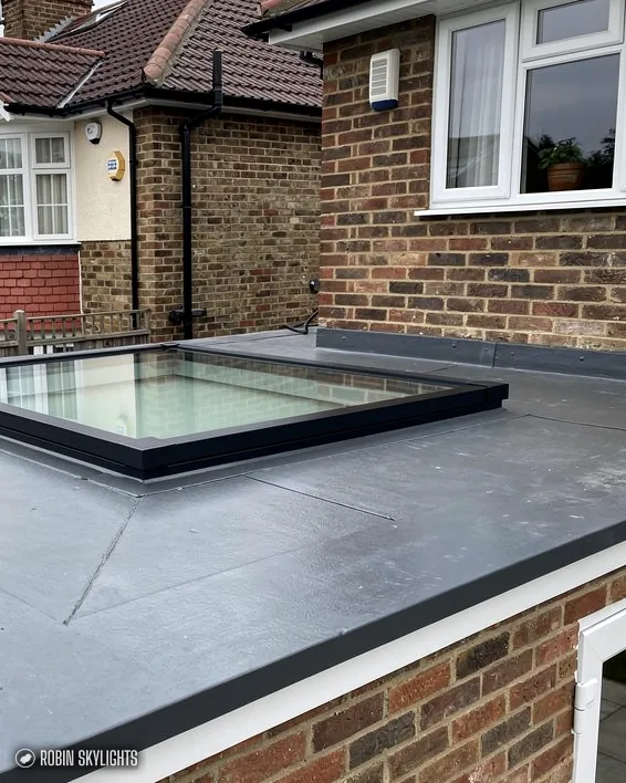 Flat rooflight on a grey flat roof by a brick house