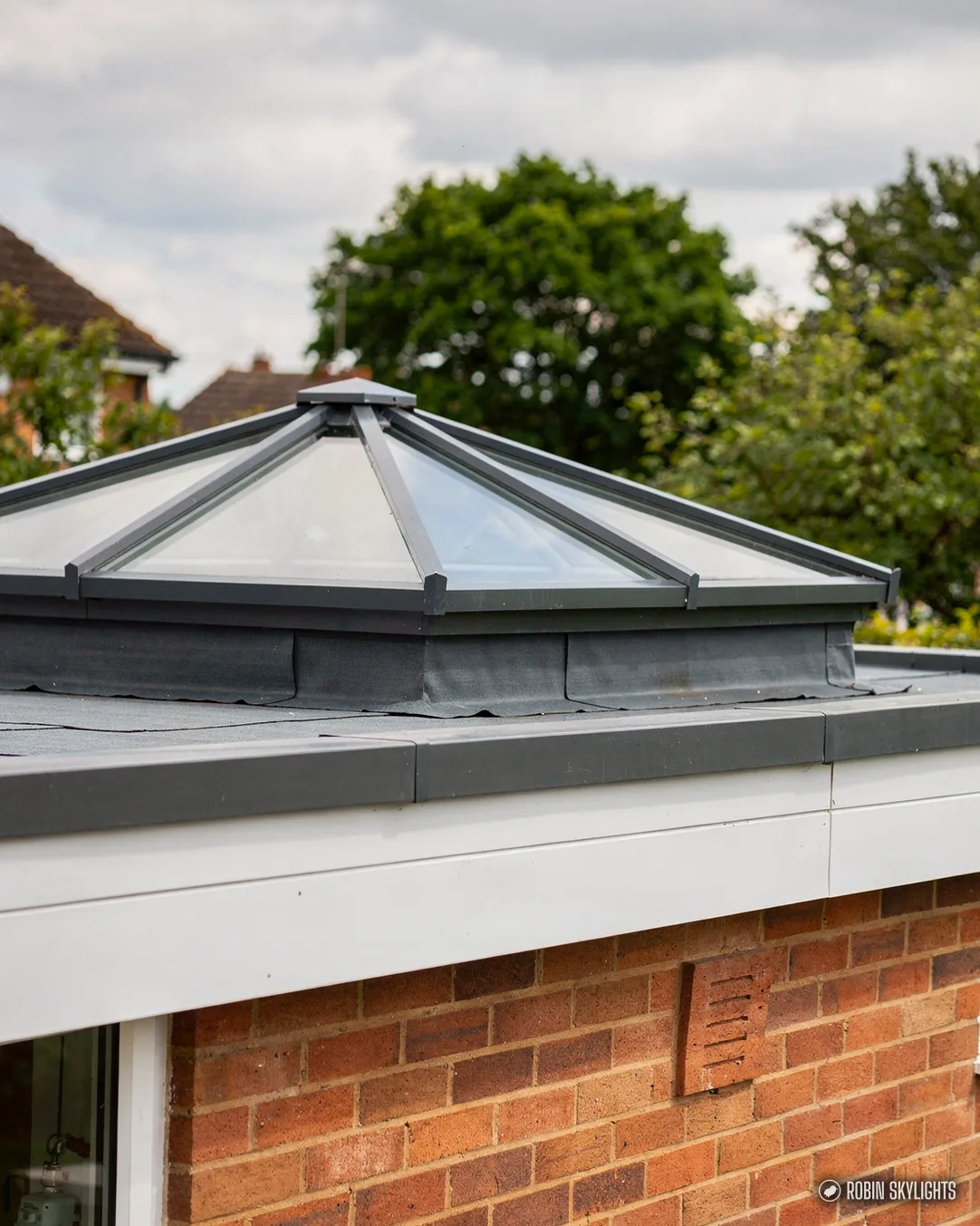 Grey roof lantern on a flat roof above a brick wall and trees