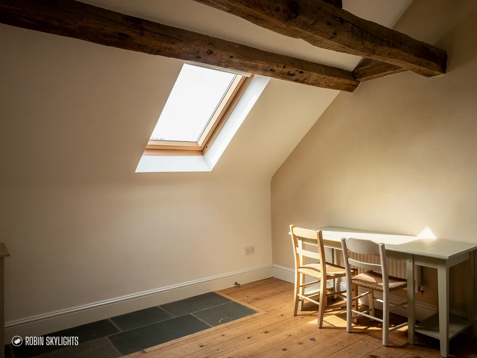 Room with a dining table and dark beam lit by a roof window