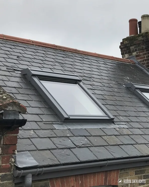 Roof window in a slate roof beside a chimney