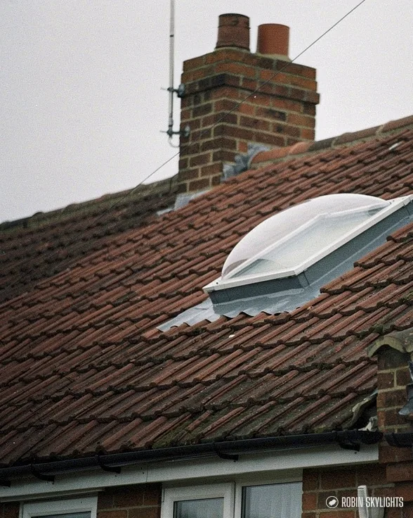 Sun tunnel dome on a tiled roof beside a brick chimney stack