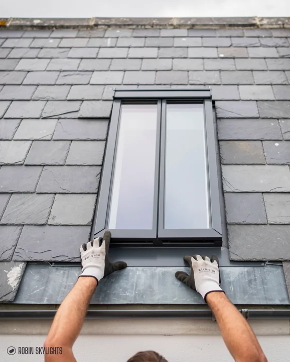 Gloved hands fitting a roof window into a slate roof